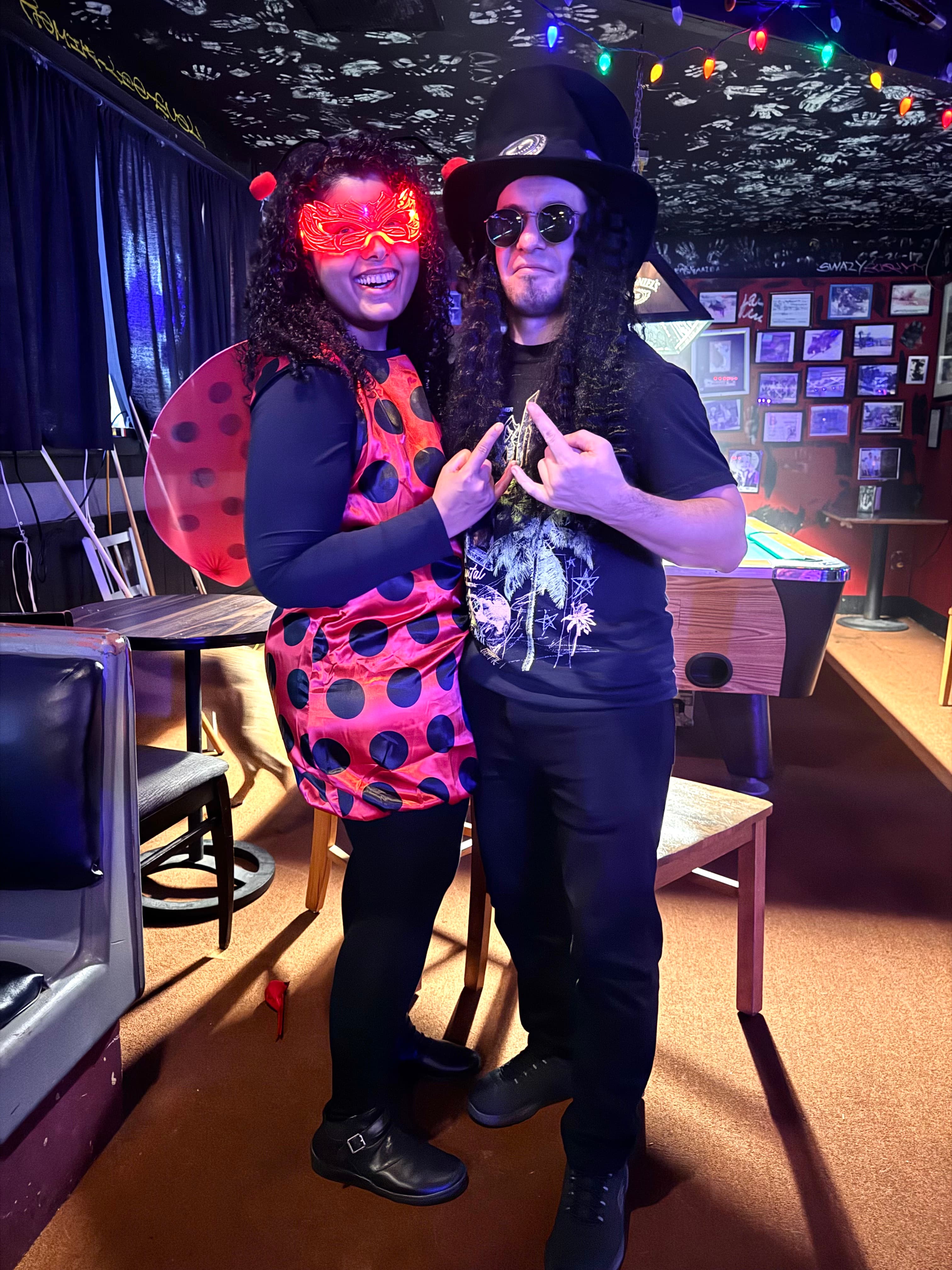 Gayatri dressed as a ladybug and Oleg as a long-haired rocker in a top hat at a Halloween party