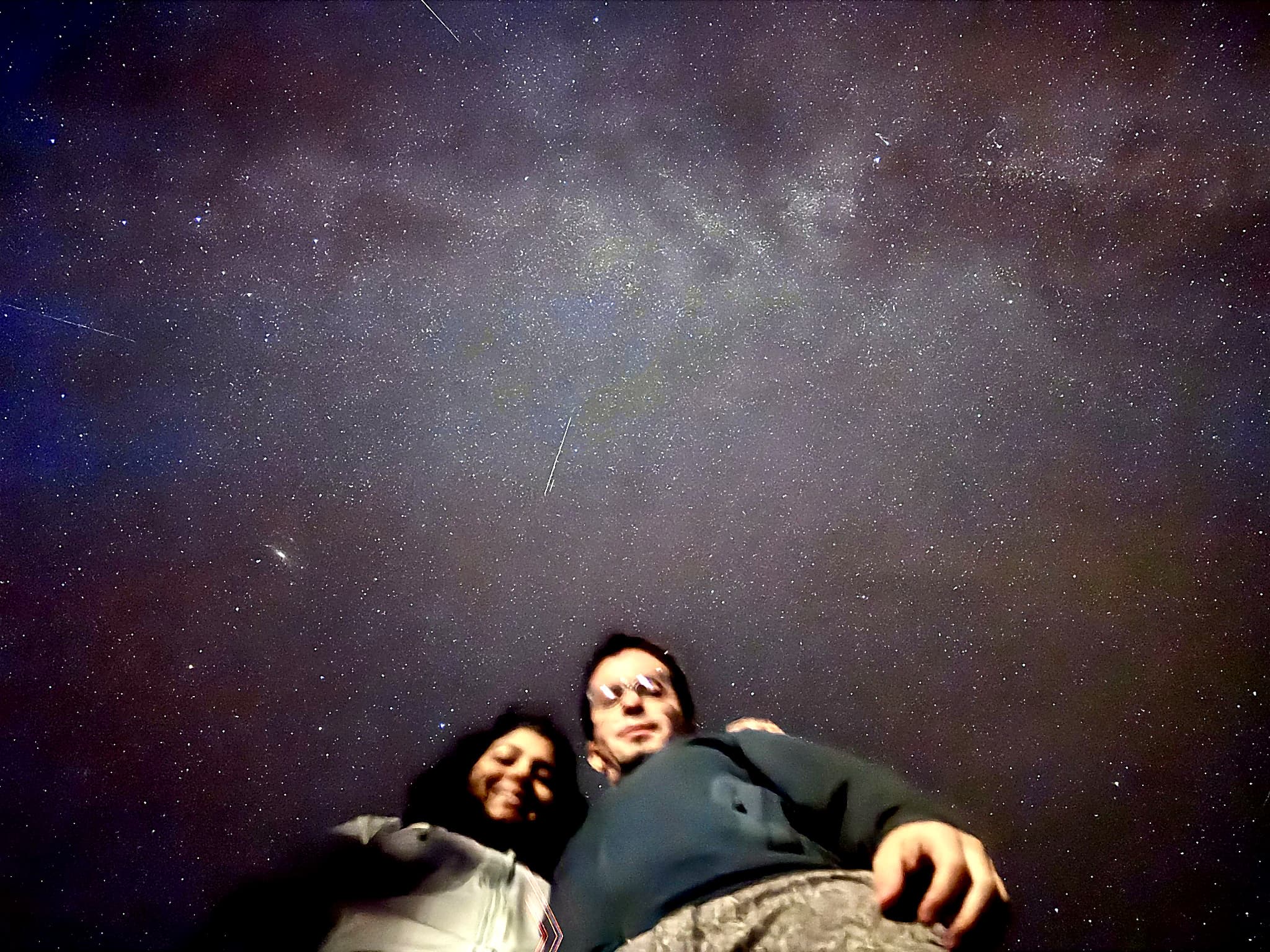Gayatri and Oleg taking a selfie beneath a star-filled night sky with the Milky Way overhead