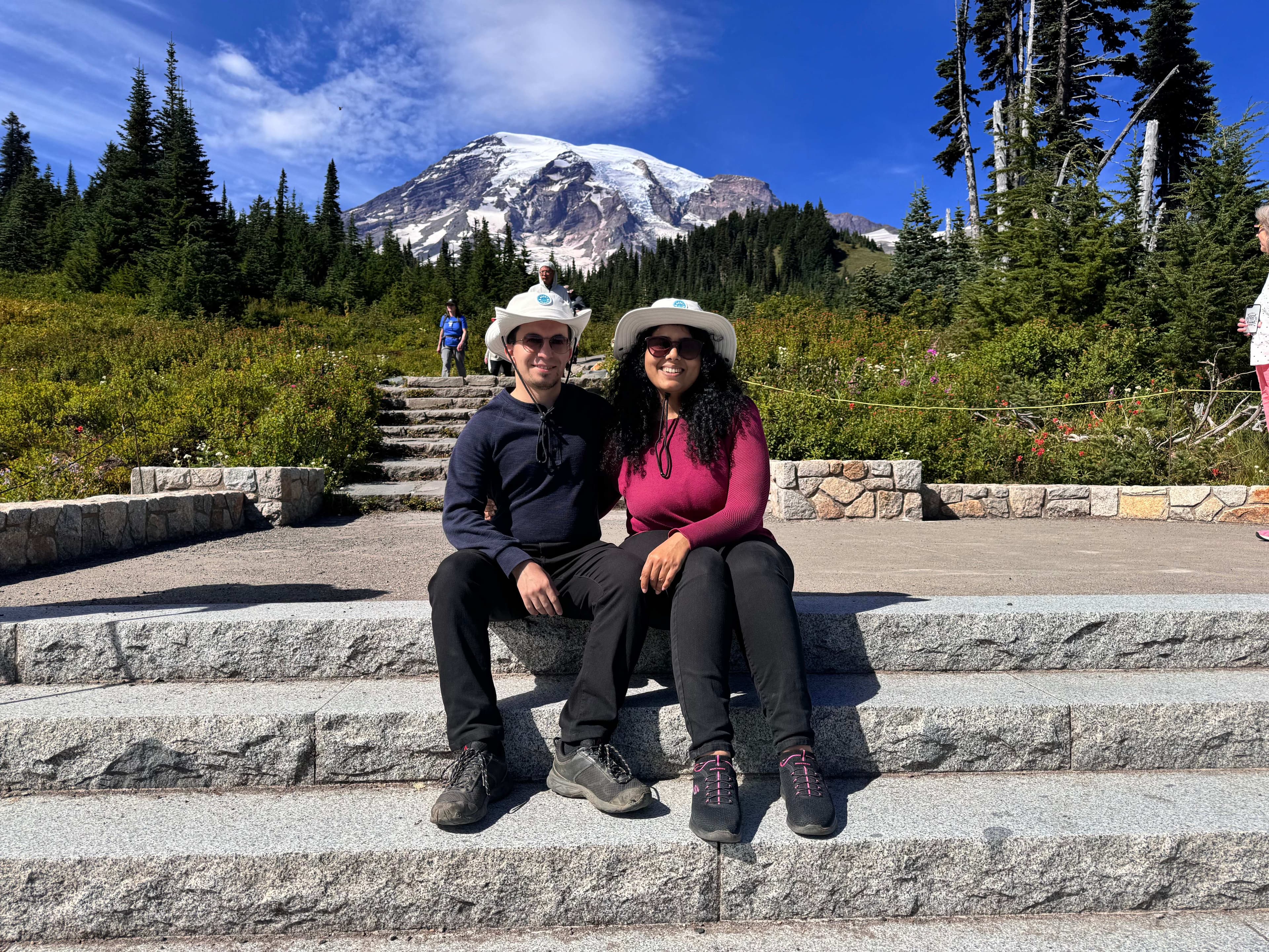 Gayatri and Oleg in sun hats sitting on stone steps below Mount Rainier